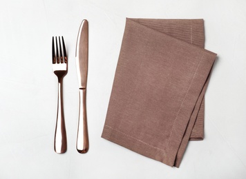 Fork, knife and napkin on light background, flat lay