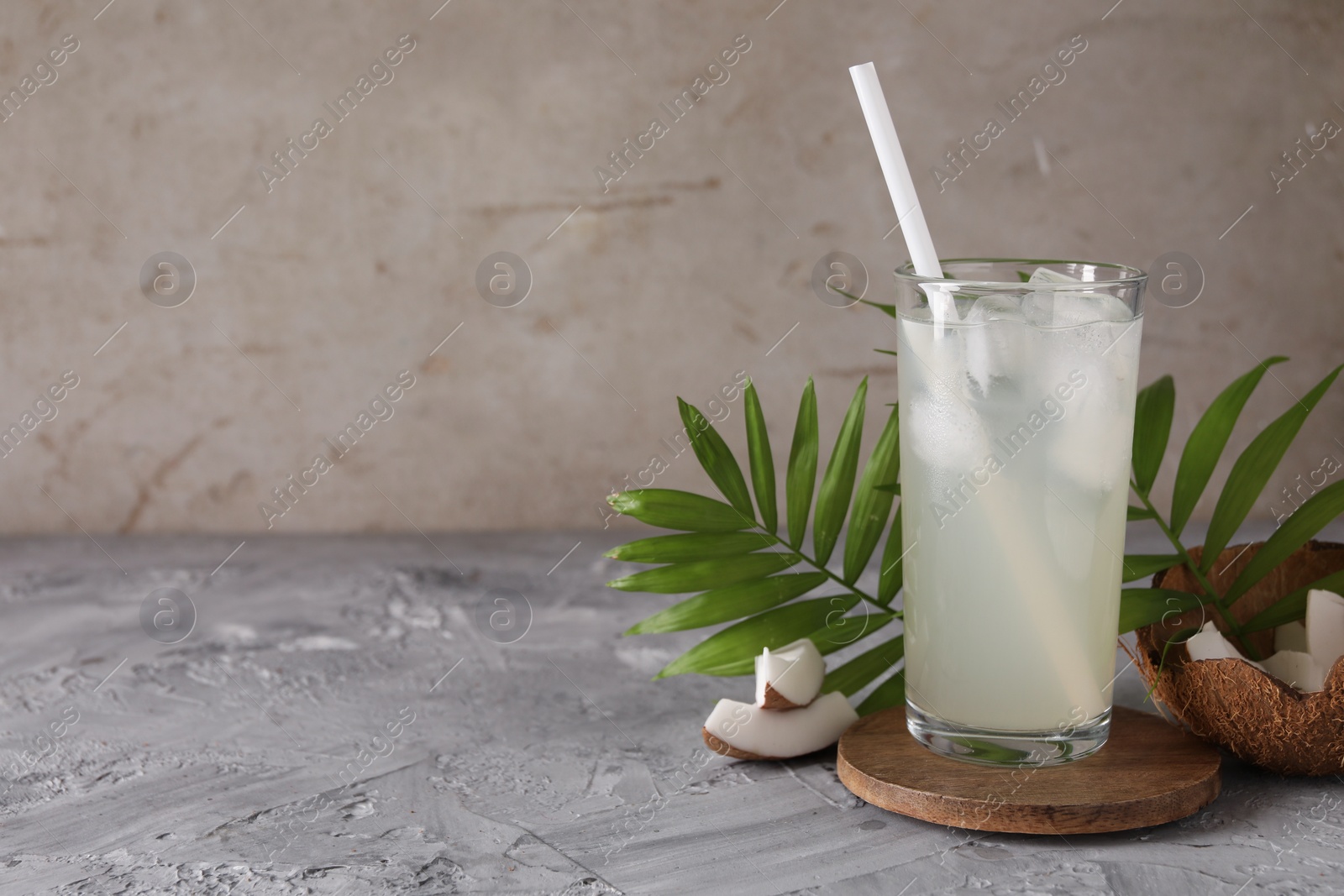 Photo of Glass of coconut water, ice cubes, leaves and nuts on grey table, space for text