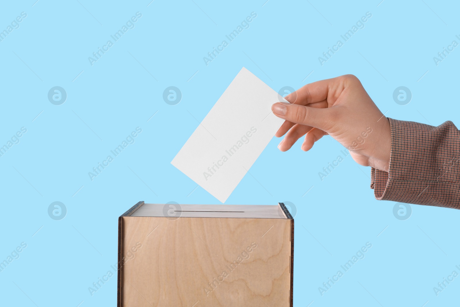 Photo of Woman putting her vote into ballot box on light blue background, closeup