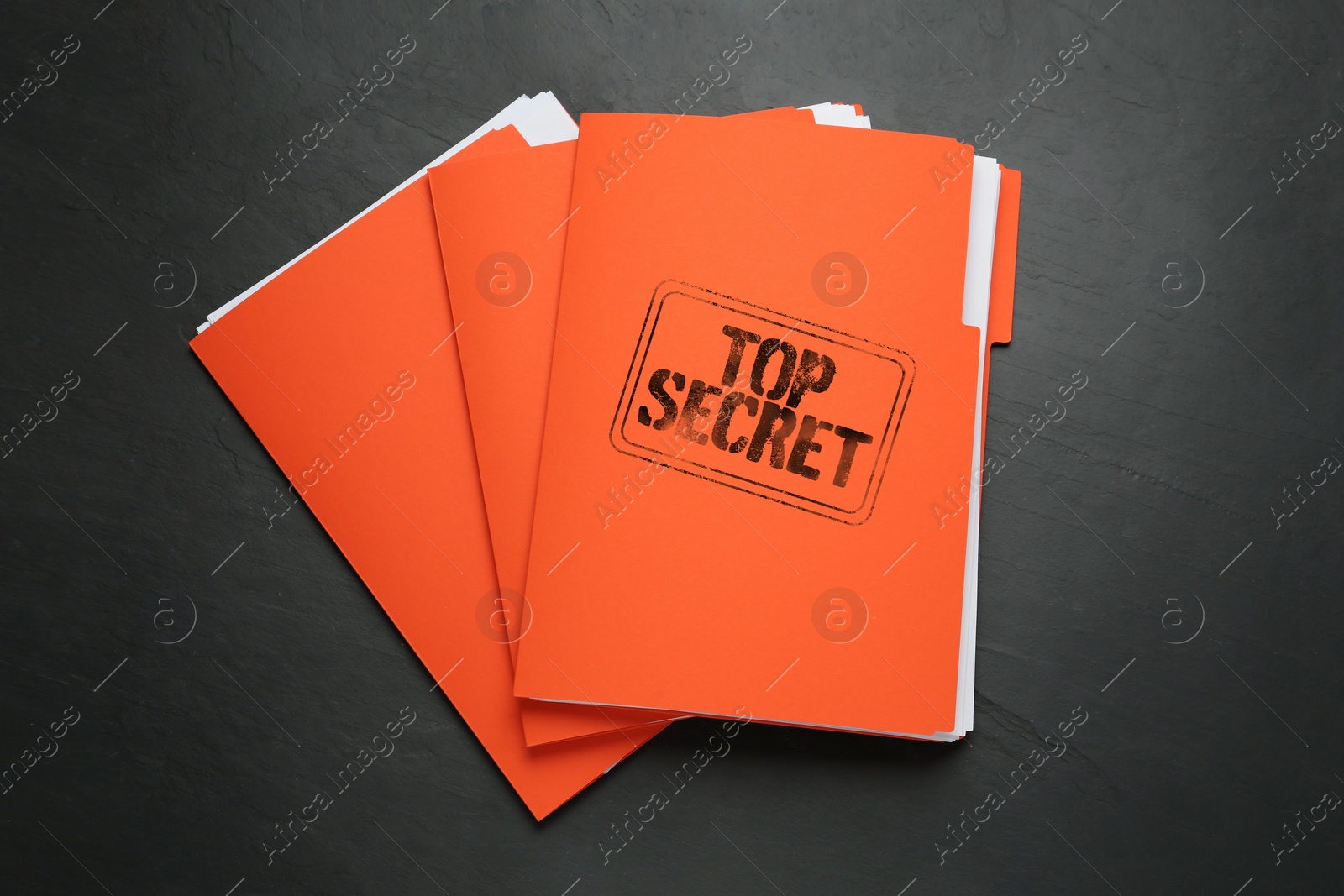 Image of Top Secret stamp. Orange files with documents on black table, top view