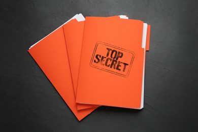 Top Secret stamp. Orange files with documents on black table, top view