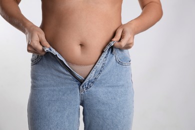 Photo of Woman trying to put on tight jeans against light background, closeup