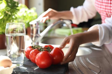 Photo of Woman with fresh tomatoes at countertop in kitchen, closeup