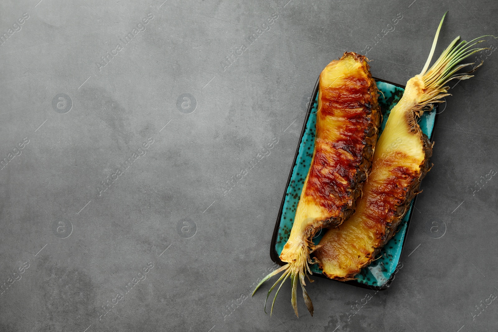 Photo of Tasty grilled pineapple pieces on grey textured table, top view. Space for text