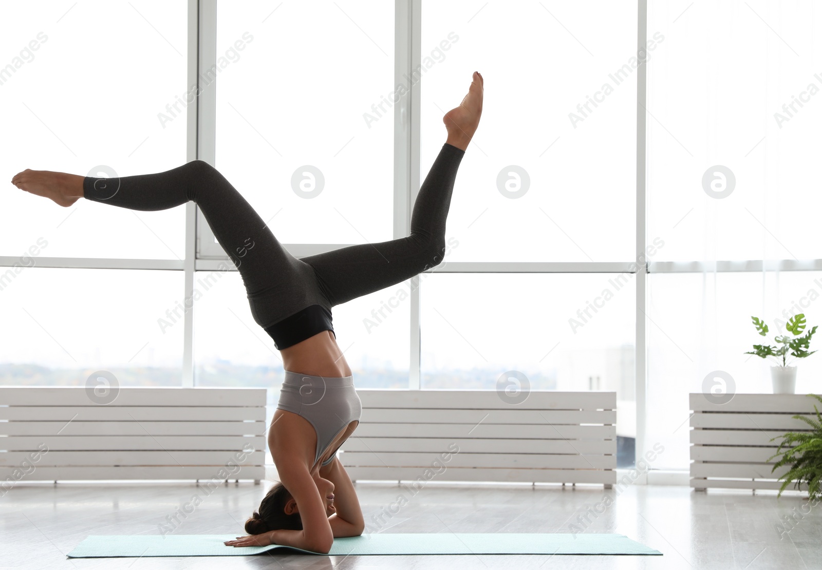 Photo of Young woman practicing headstand with splits in yoga studio