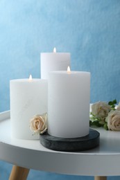 Photo of Burning candles and beautiful roses on white table near light blue wall