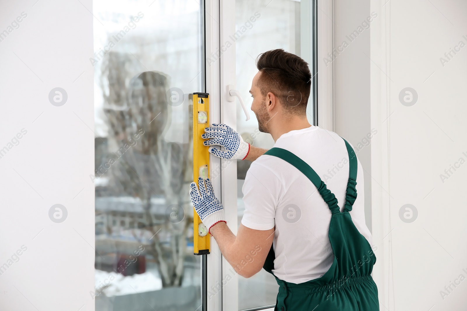 Photo of Construction worker using bubble level while installing window indoors