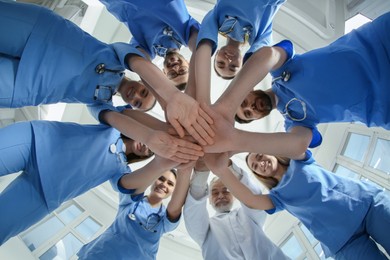 Photo of Doctor and interns stacking hands together indoors, bottom view