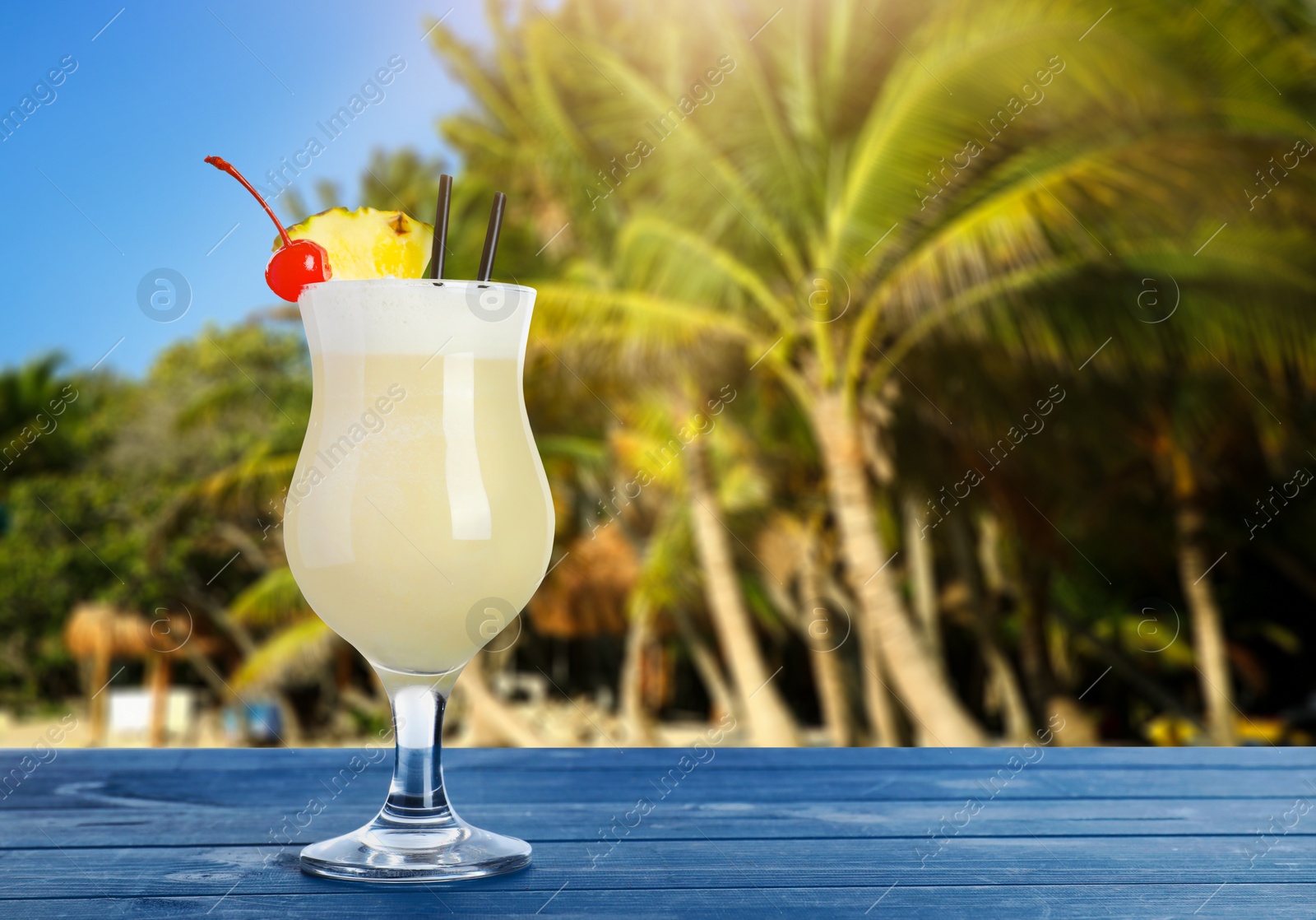 Image of Tasty pineapple cocktail in glass on blue wooden table at beach, space for text