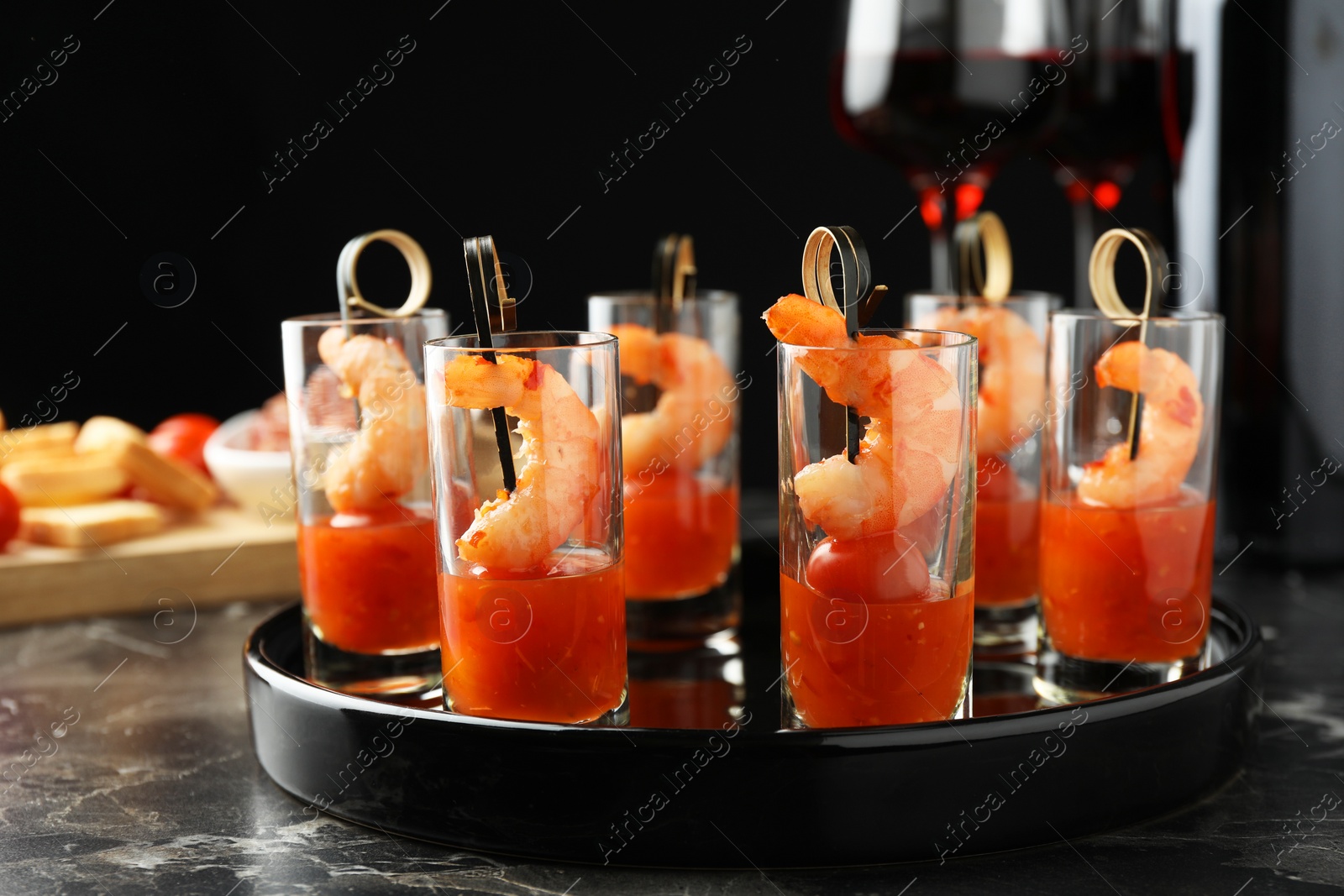 Photo of Tasty canapes with shrimps, tomatoes and sauce in shot glasses on black marble table, closeup