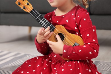Photo of Little girl playing toy guitar at home, closeup