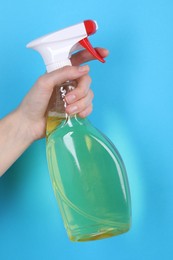 Photo of Woman holding plastic spray bottle on light blue background, closeup