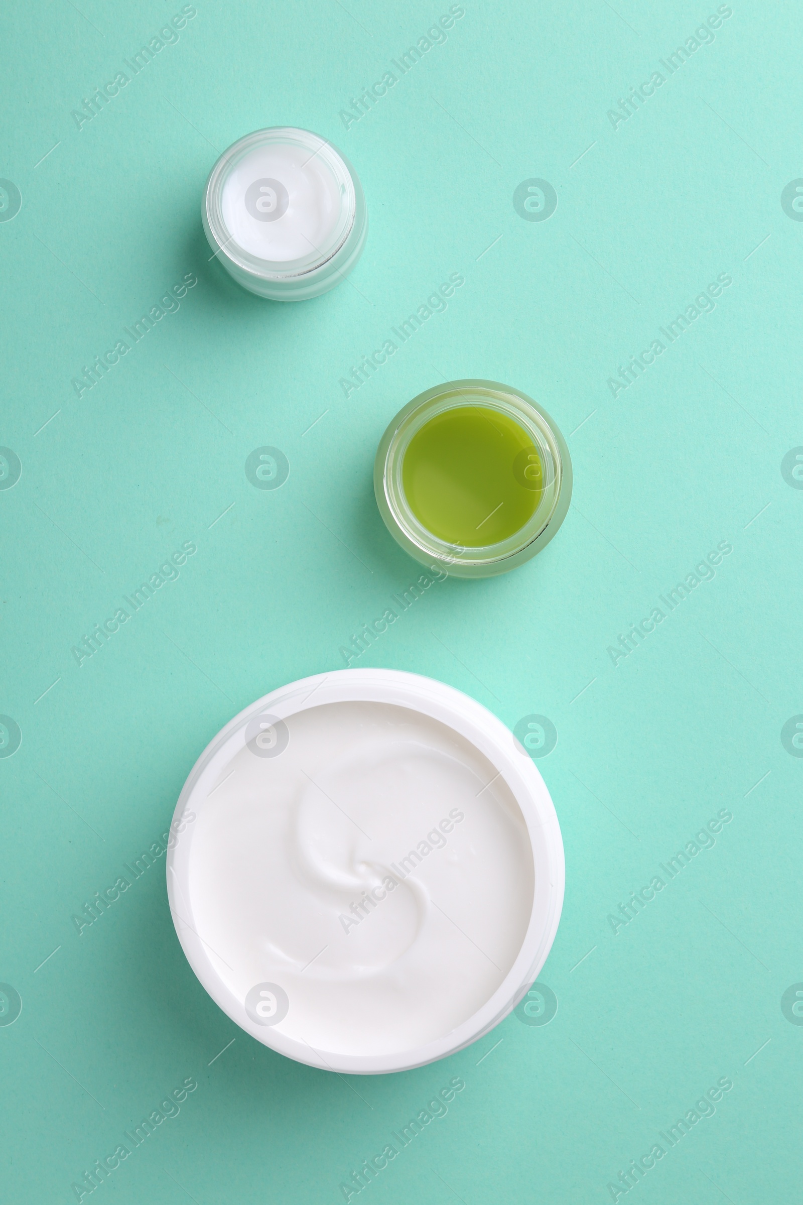 Photo of Moisturizing cream in open jars on turquoise background, flat lay. Body care products