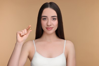 Beautiful young woman with vitamin pill on beige background