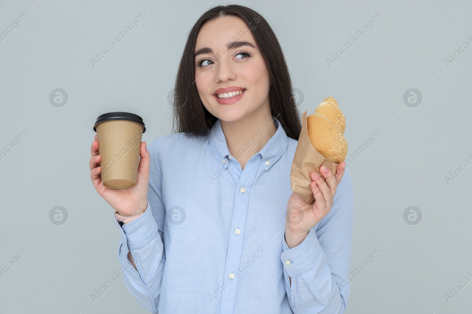 Photo of Young female intern with croissant and cup of drink on grey background