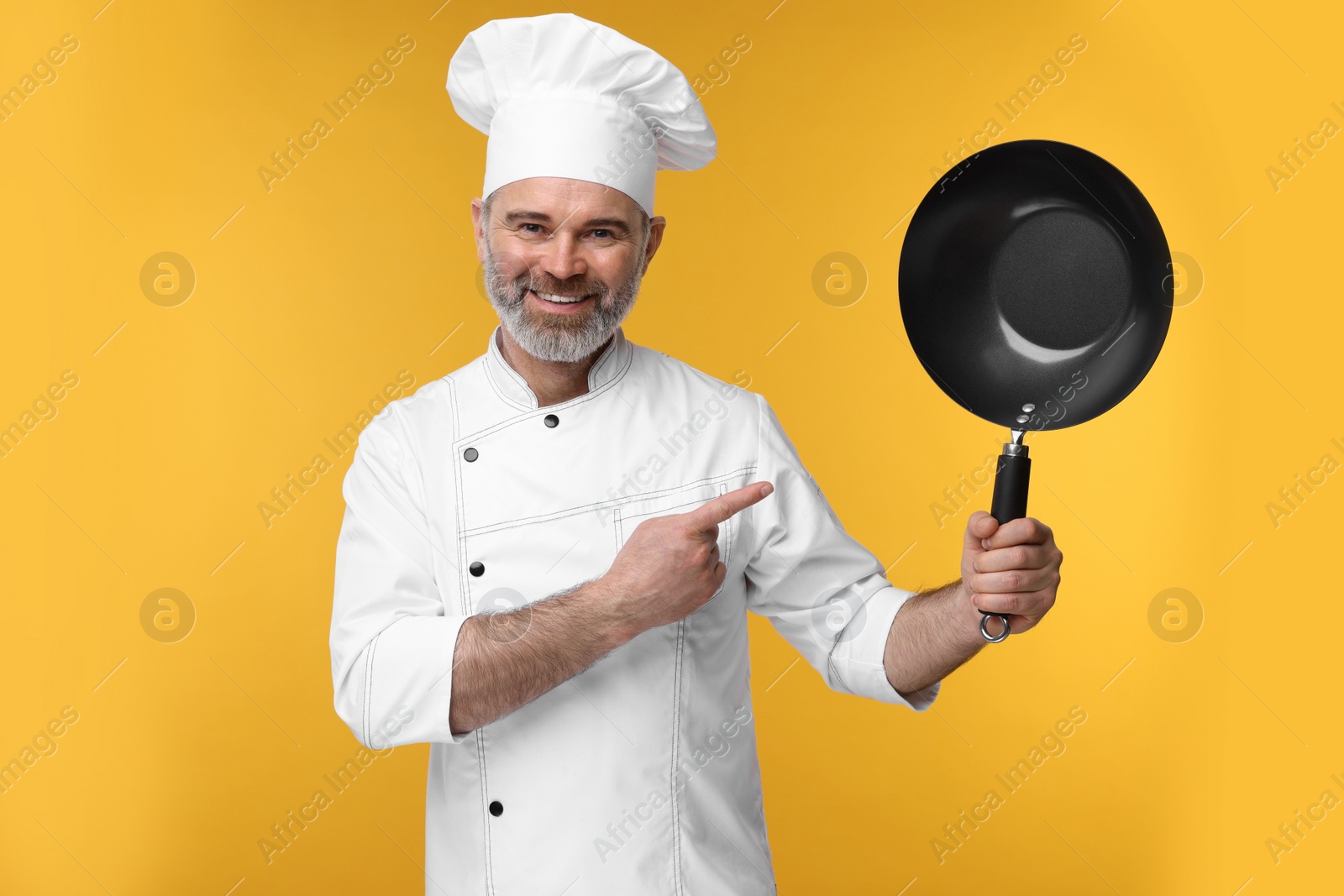 Photo of Happy chef in uniform pointing at wok on orange background