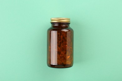 Bottle with vitamin capsules on turquoise background, top view