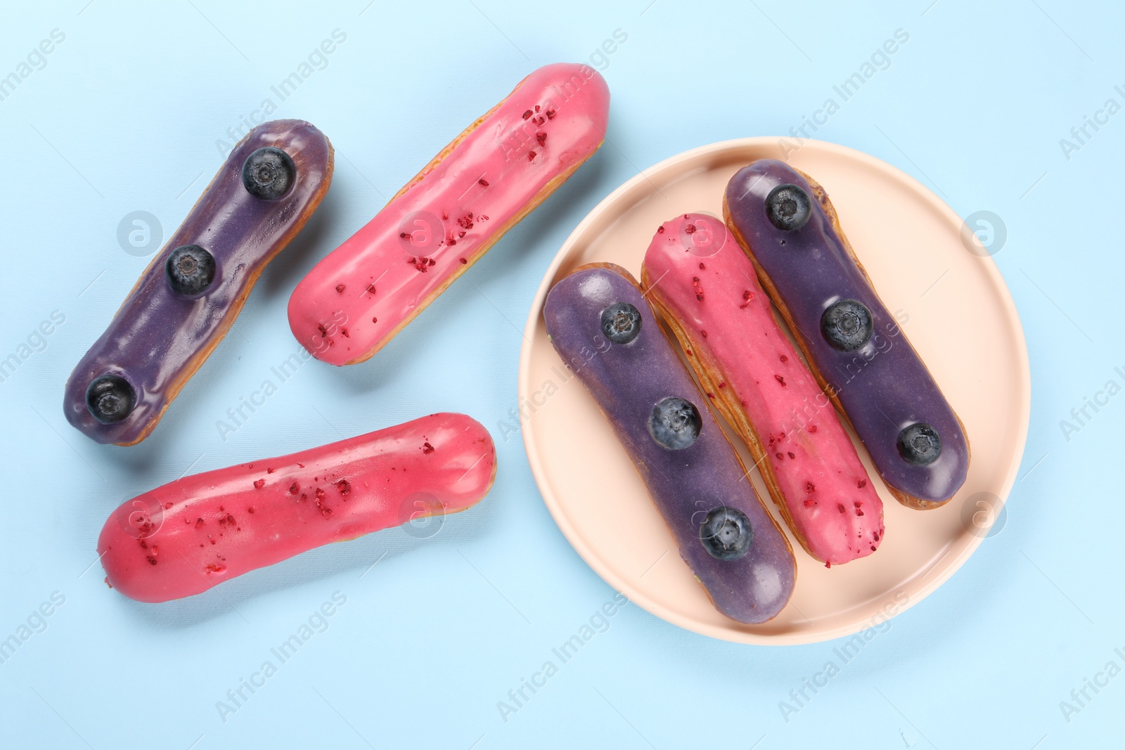 Photo of Delicious eclairs covered with glaze on light blue background, top view