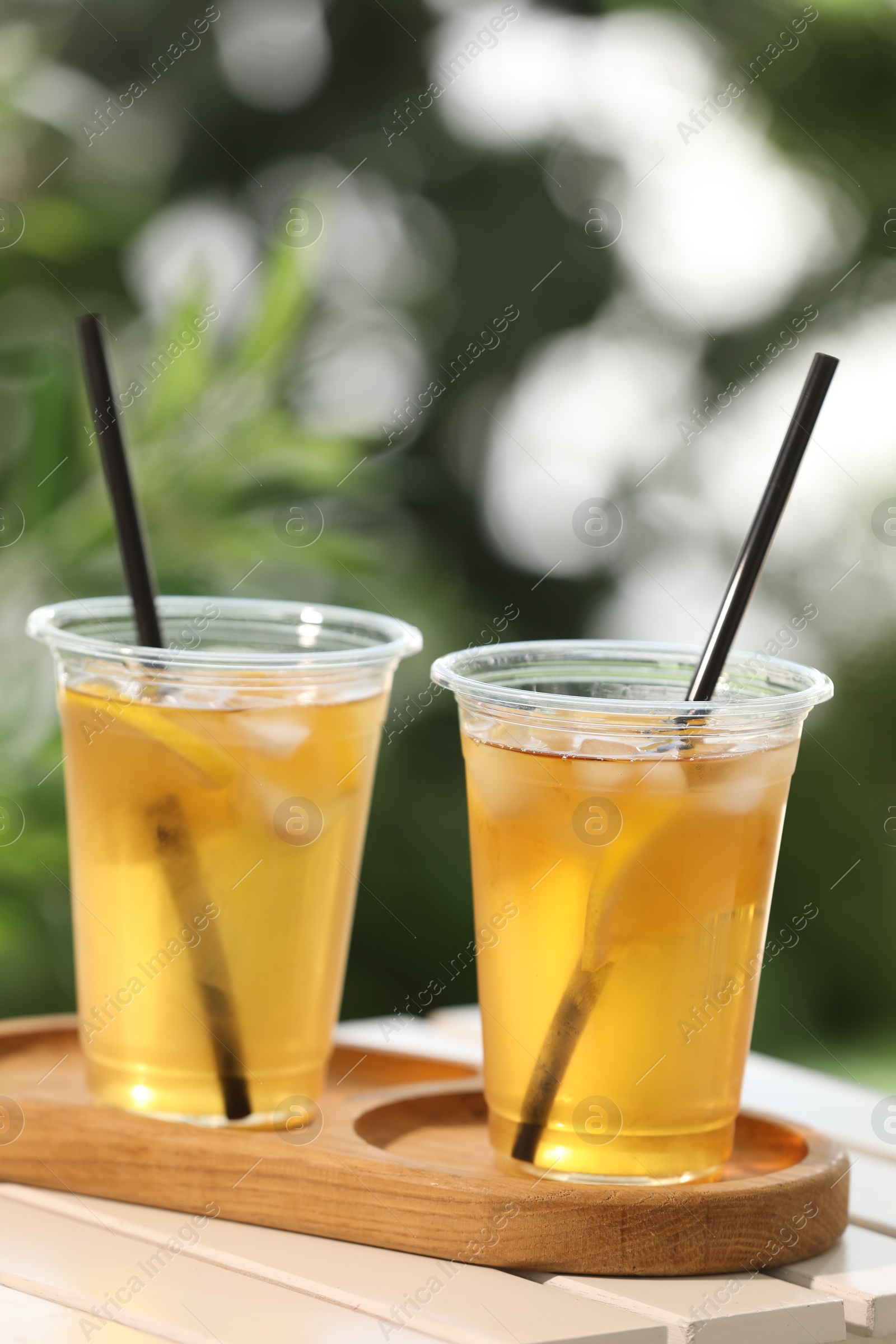 Photo of Plastic cups of tasty iced tea with lemon on white wooden table against blurred background