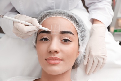 Photo of Young woman getting prepared for procedure of permanent eyebrow makeup in tattoo salon