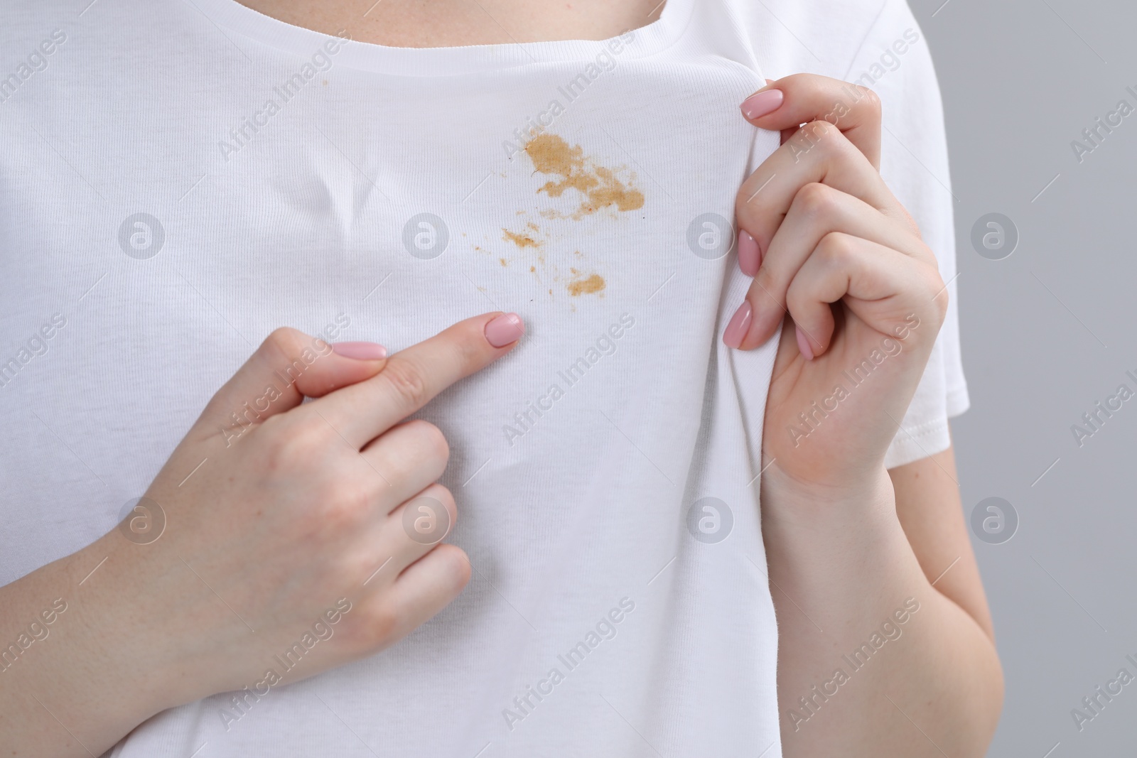 Photo of Woman showing stain on her t-shirt against light grey background, closeup