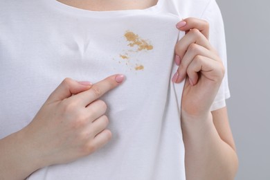 Woman showing stain on her t-shirt against light grey background, closeup