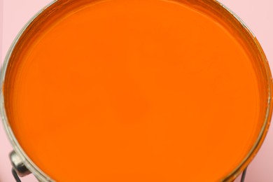 Bucket of orange paint on pink background, closeup
