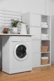 Laundry room interior with modern washing machine and shelving unit near white wall