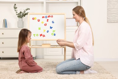 Photo of Mom teaching her daughter alphabet with magnetic letters at home