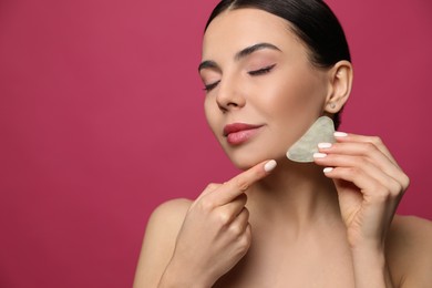 Photo of Beautiful young woman doing facial massage with gua sha tool on pink background, closeup