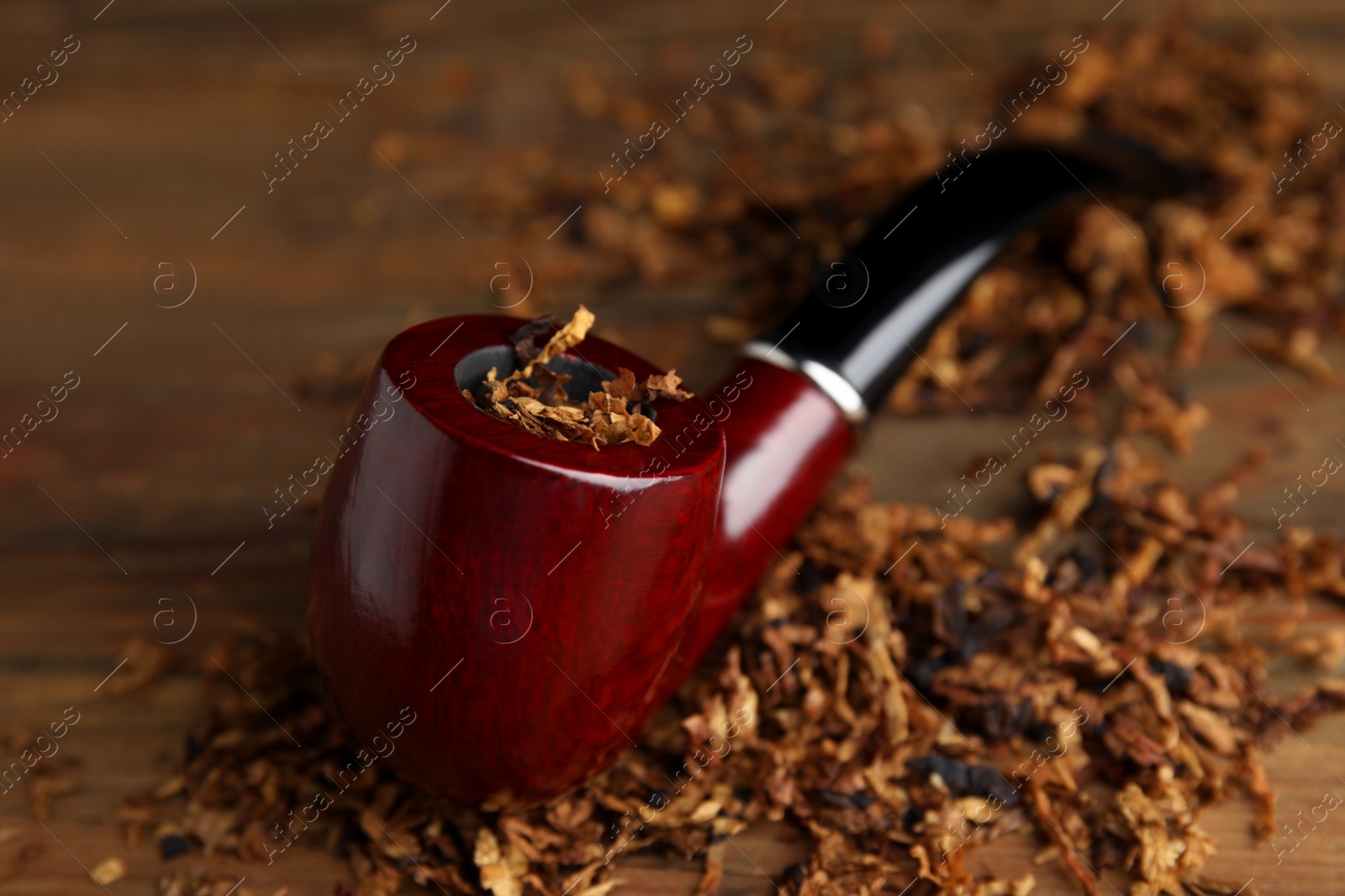 Photo of Smoking pipe and dry tobacco on wooden table, closeup