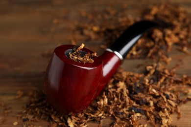 Smoking pipe and dry tobacco on wooden table, closeup