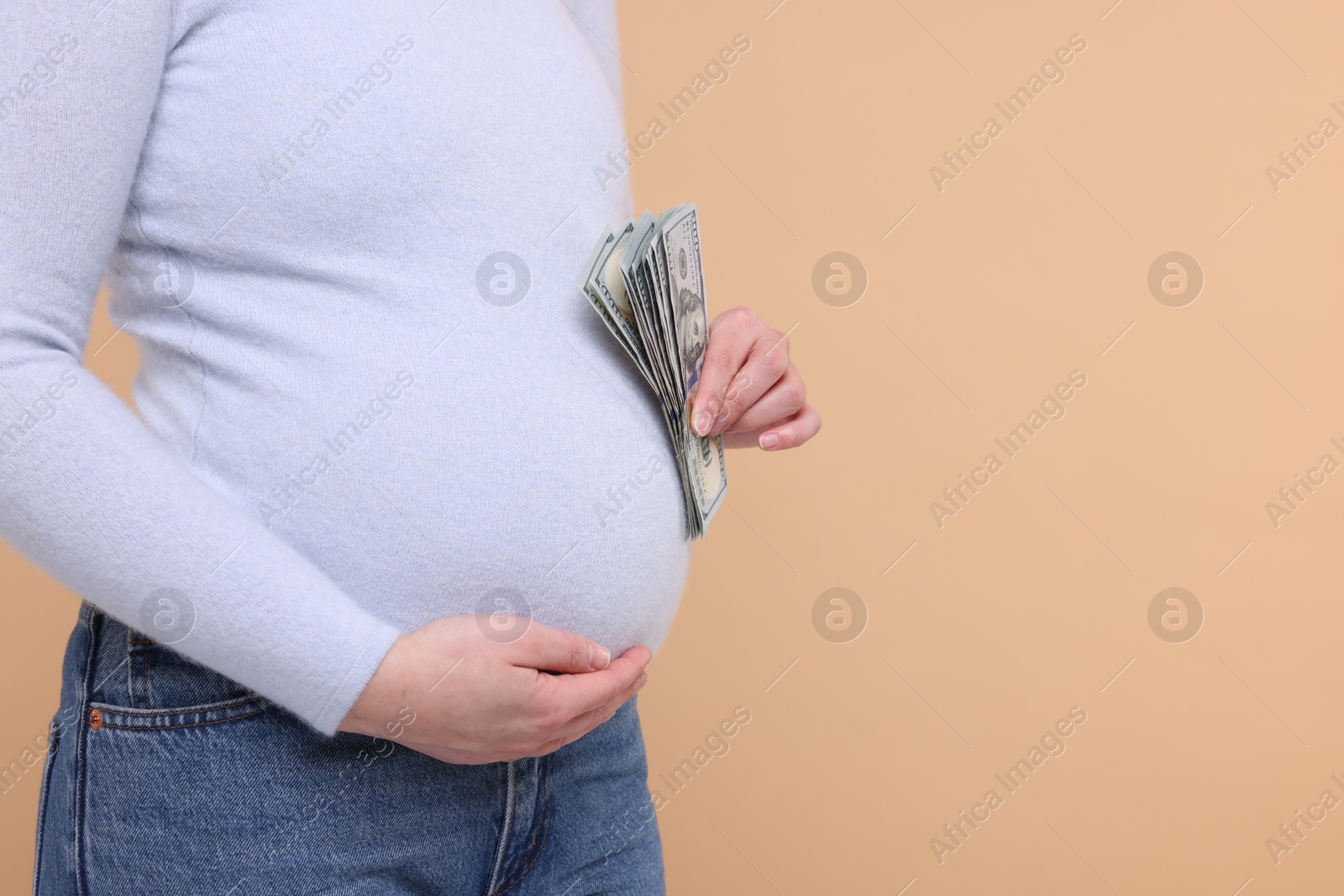 Photo of Surrogate mother. Pregnant woman with dollar banknotes on beige background, closeup. Space for text