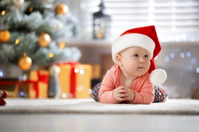 Photo of Little baby wearing Santa hat on floor indoors. First Christmas