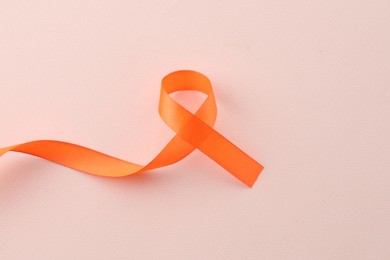Orange awareness ribbon on beige background, top view