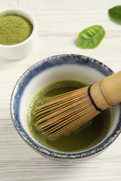 Photo of Cup of fresh matcha tea with bamboo whisk on white wooden table, above view