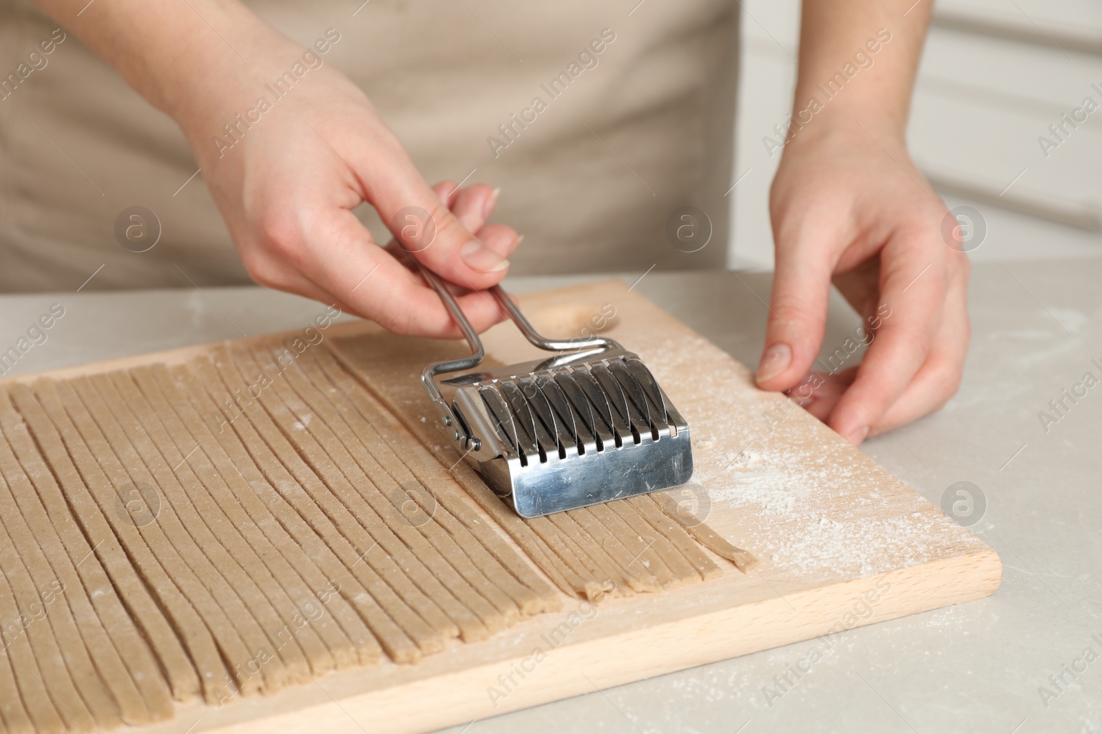 Photo of Woman making soba (buckwheat noodles) at light marble table, closeup