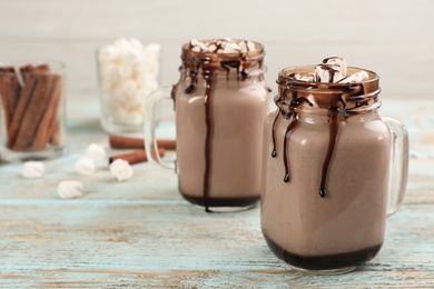Photo of Jars of chocolate milk with marshmallows on light wooden table. Space for text
