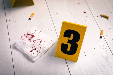 Photo of Bloody napkin, stubs and crime scene marker on white wooden table