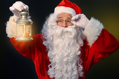 Photo of Santa Claus holding Christmas lantern with burning candle on dark background