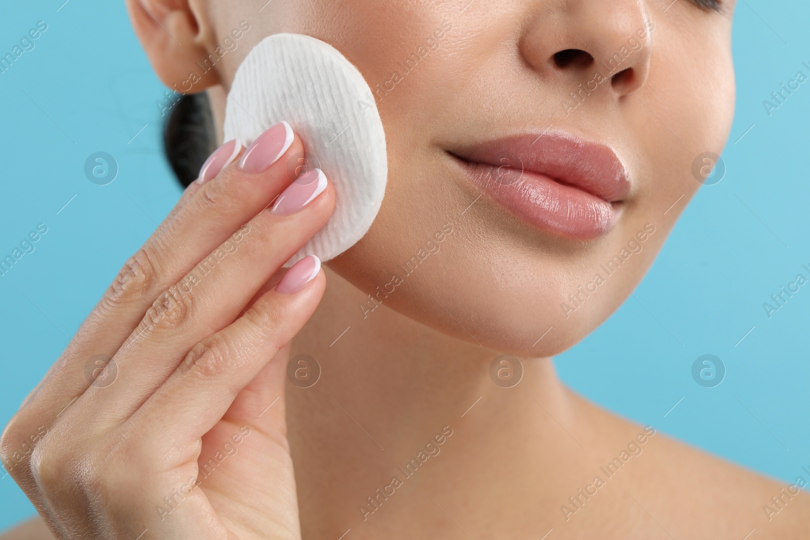 Photo of Beautiful woman removing makeup with cotton pad on light blue background, closeup