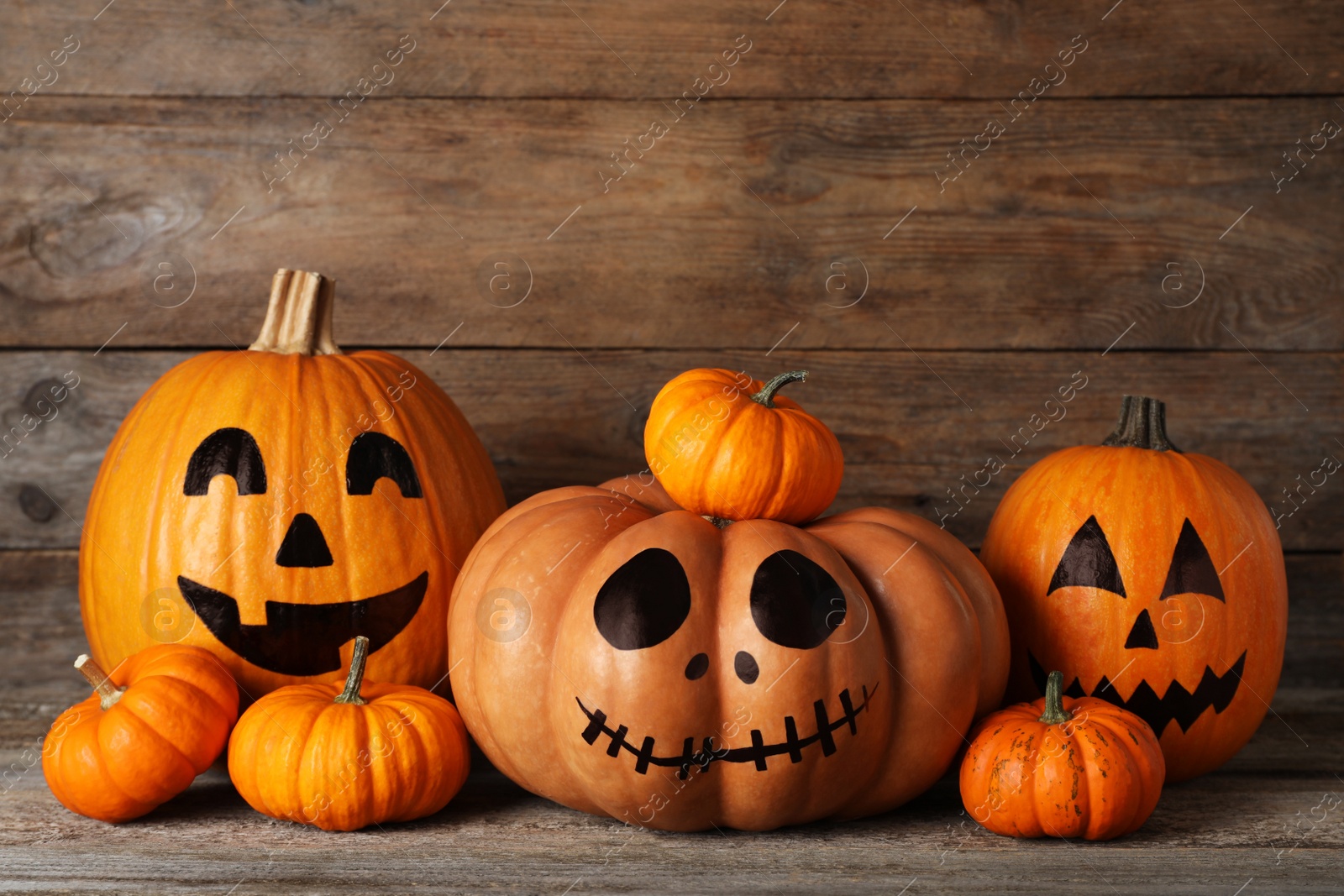 Photo of Orange pumpkins and three with drawn spooky faces on wooden table. Halloween celebration