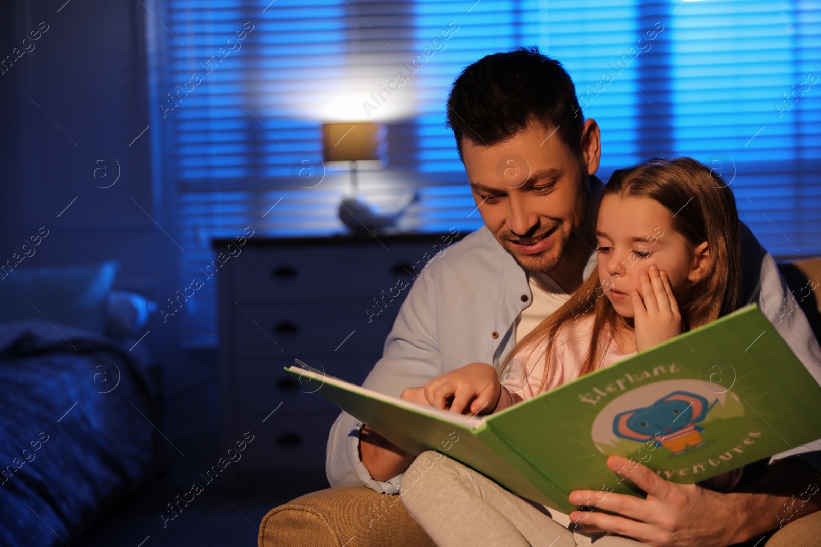 Photo of Father reading bedtime story to his daughter at home