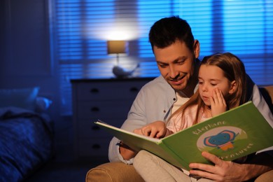 Photo of Father reading bedtime story to his daughter at home