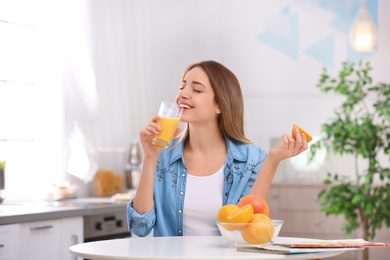 Photo of Beautiful young woman drinking fresh orange juice in kitchen. Healthy diet