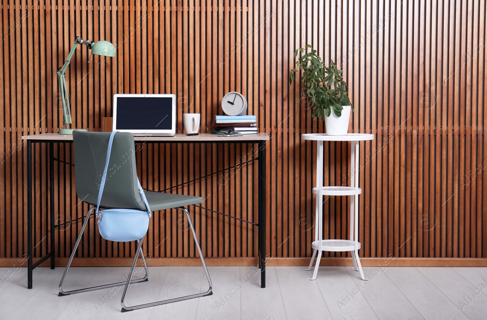 Photo of Stylish workplace interior with laptop on table near wooden wall. Space for text