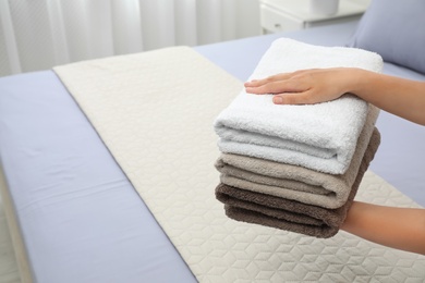 Photo of Woman putting soft clean towels on bed indoors, closeup. Space for text