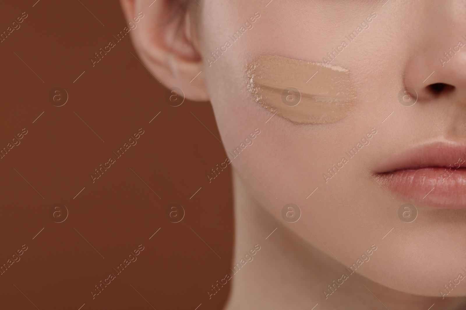 Photo of Teenage girl with swatch of foundation on face against brown background, closeup