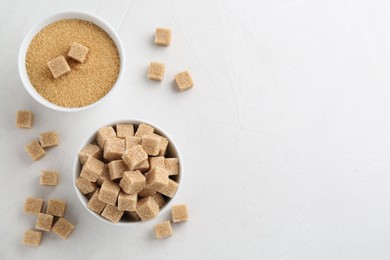 Photo of Brown granulated sugar and cubes on white textured table, flat lay. Space for text