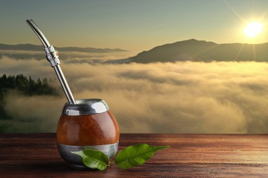 Calabash with mate tea and bombilla on wooden table and beautiful view of mountain landscape, space for text